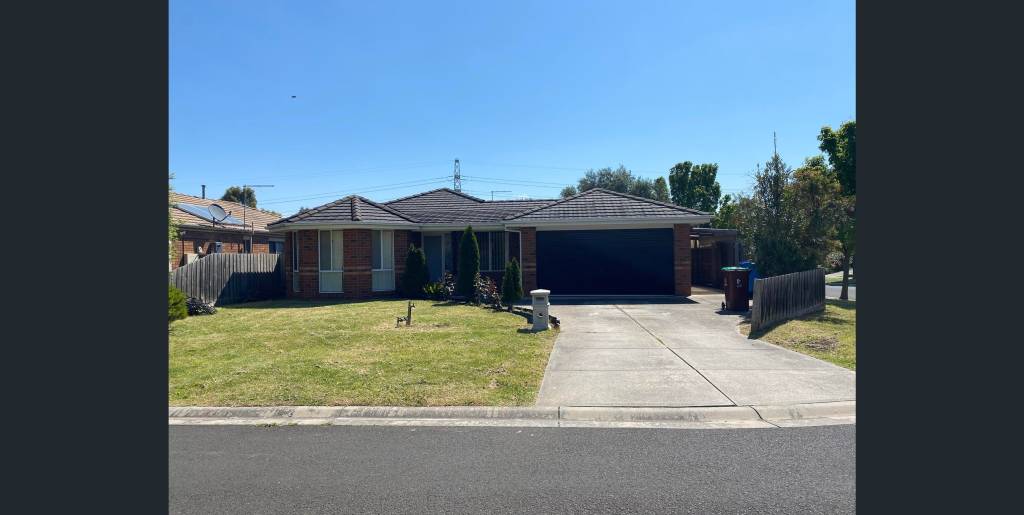 A front view of a modern brick house with a driveway and a green lawn under a clear blue sky.